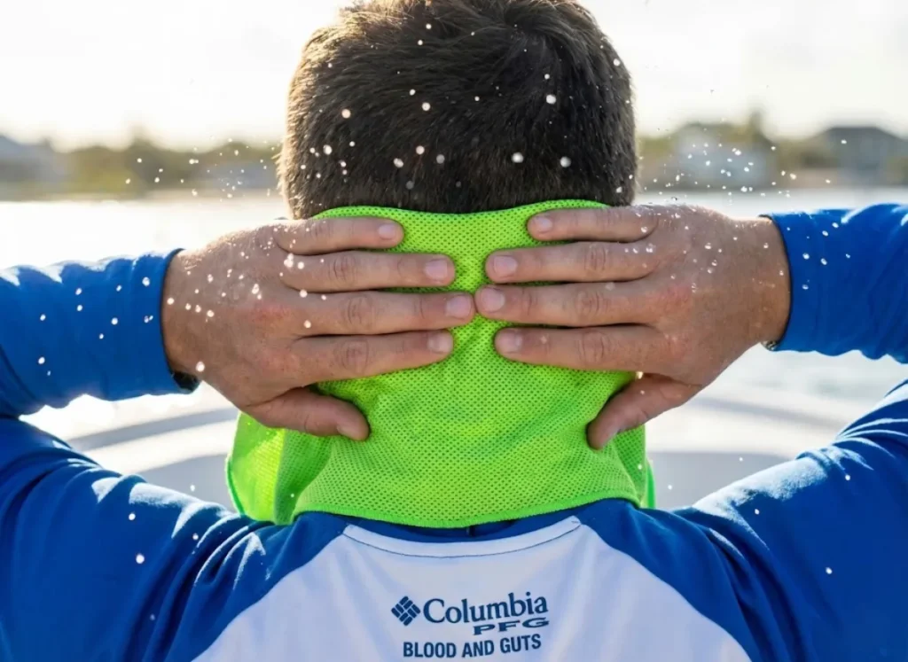 Hands applying a wet cooling towel to an angler's neck, capturing water droplets and the texture of the cooling gear for rapid temperature reduction.