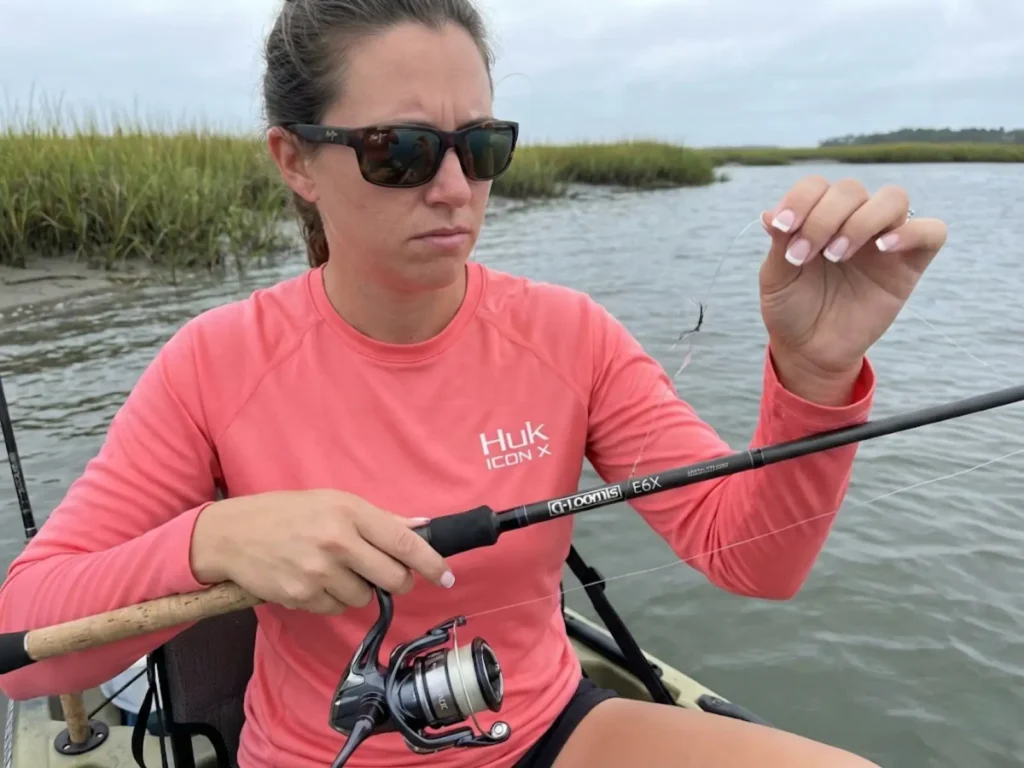 Female kayak angler examining broken fishing line after knot failure on coastal estuary