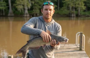 Handling Catfish Spines: The Size-by-Size Safety Guide Angler demonstrating proper catfish handling grip behind spines on a river dock