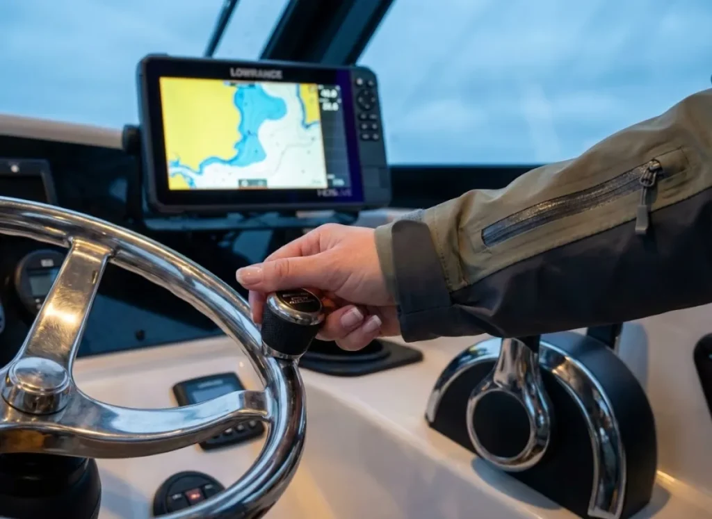 A view from the captain's chair showing a hand adjusting a Mercury kicker motor throttle with glowing Lowrance electronics in the background.