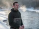 Layering Base Layers for Maximum Warmth A professional angler standing in a winter river wearing high-end waders and a textured merino wool base layer, breath visible in the cold air.