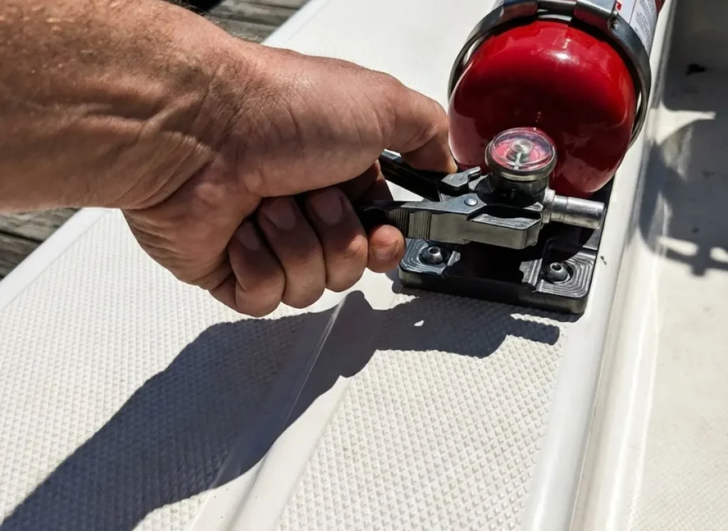 Close up of a heavy-duty metal quick-release fire extinguisher bracket being secured on a fishing boat.
