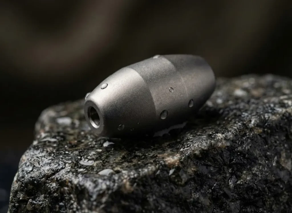 Macro shot of a high-density tungsten fishing weight resting on a wet granite rock.
