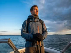 Read Cloud Formations to Predict Storms Professional angler in Simms gear standing on a boat bow, scanning a dramatic sky where cirrus clouds transition into storm clouds, symbolizing weather prediction.