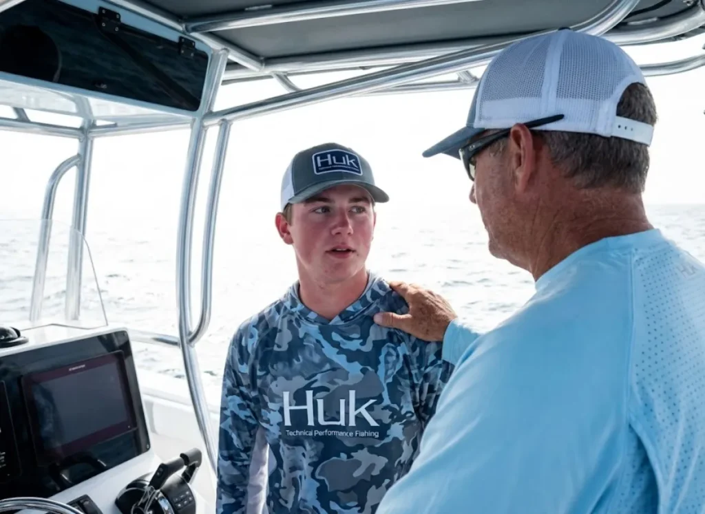 A boat captain conducting a wellness check on a crew member, examining eyes and skin tone to differentiate between heat exhaustion and heat stroke.