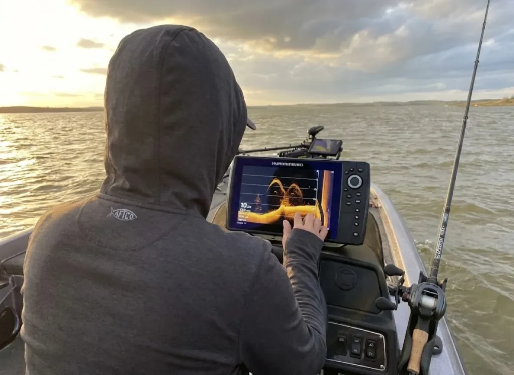 Angler studying fish finder showing suspended spotted bass over deep reservoir structure