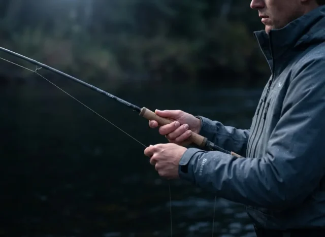 use-lateral-line-system-advantage Close-up of a professional angler in a Simms jacket gripping a bending G. Loomis rod at dusk, highlighting the tactile sensation of a fish strike in low light.