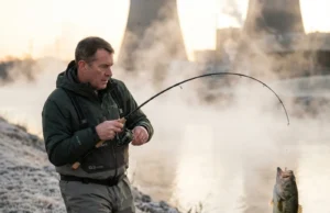 Why Warm Water Discharges Are Winter Fishing Gold Angler fighting bass at steaming power plant discharge in winter dawn light