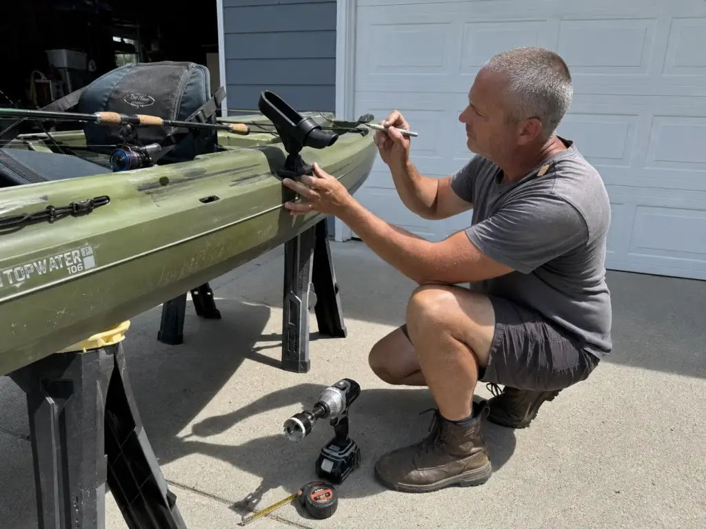 Angler dry-fitting a rod holder on a kayak in a driveway before drilling any holes