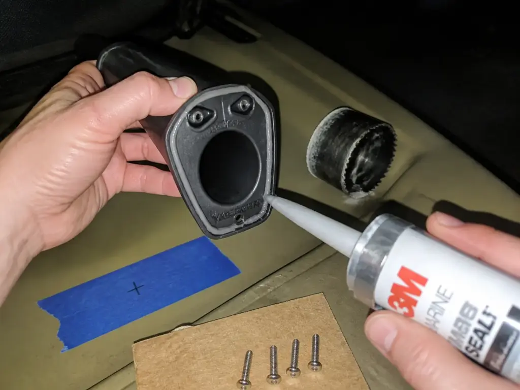 Hands laying marine sealant under a flush mount rod holder flange during a kayak install