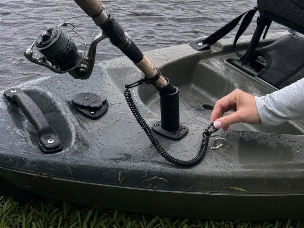 Rod leash clipped to a pad eye beside a plastic flush mount rod holder on a kayak deck