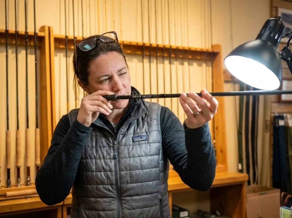 Angler inspecting graphite fly rod blank for warping under bright light 