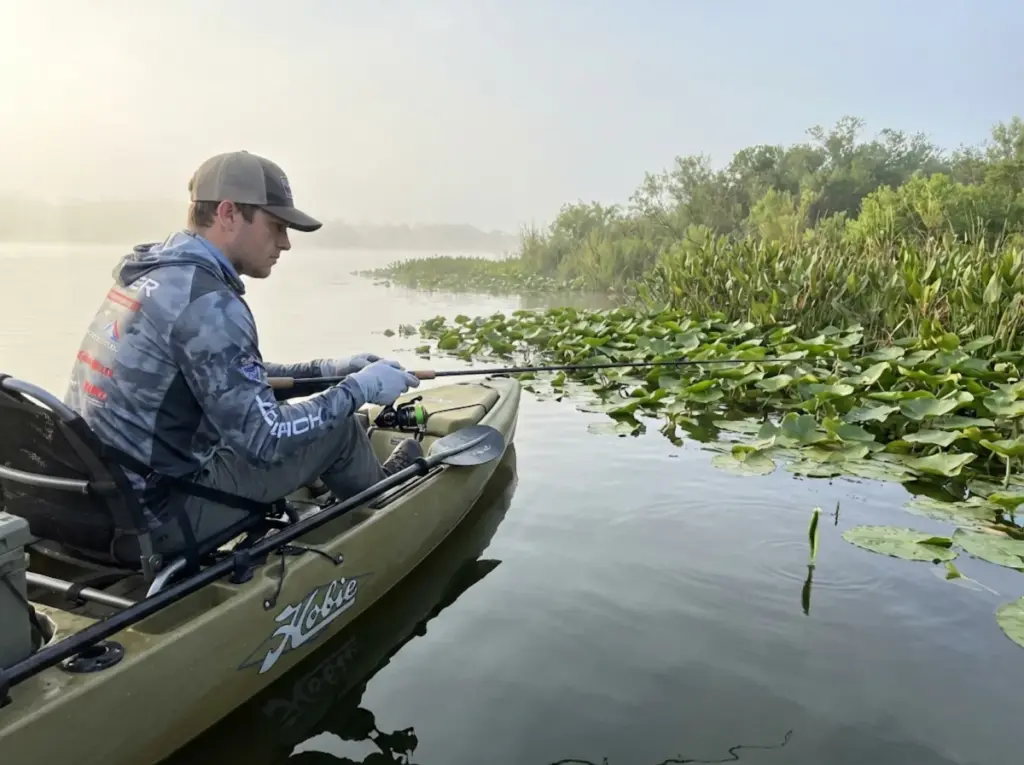 Kayak angler pausing soft plastic lure presentation near lily pads