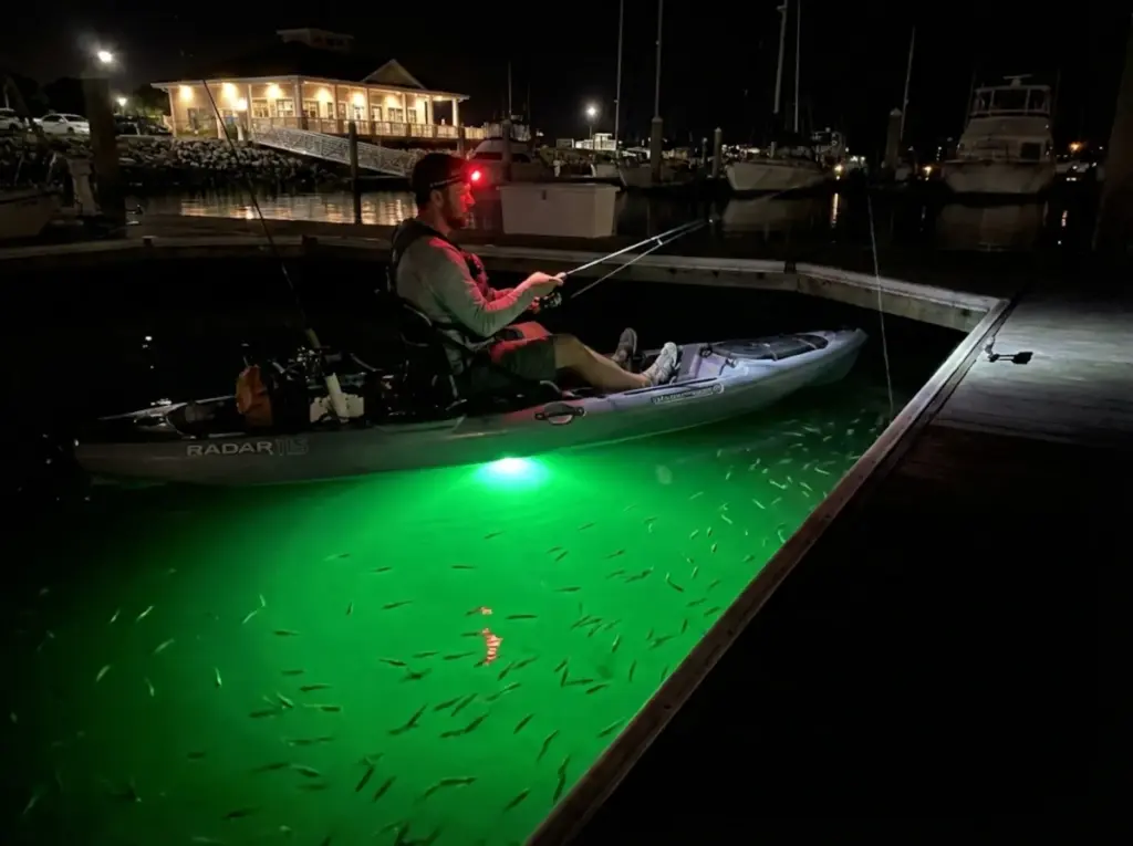 Night angler fishing near dock with green underwater light attracting baitfish