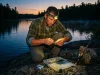 Night Fishing Headlamps That Won’t Spook the Bite Angler in a headlamp rigging tackle at dusk on a rocky bank before night fishing