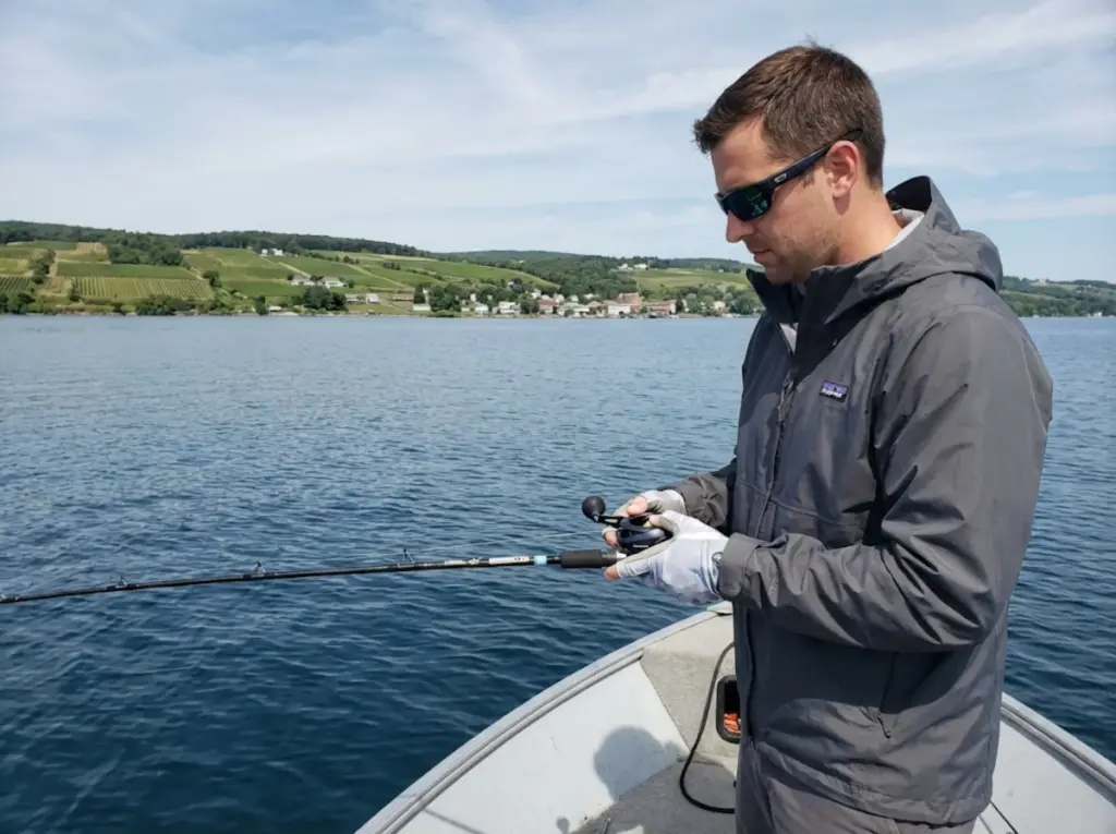 Angler vertical jigging for lake trout on Seneca Lake with vineyards visible on shore