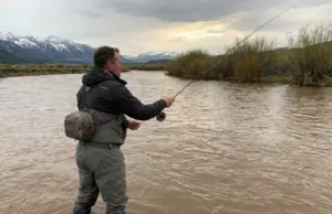 How to Fish Spring Runoff in High Muddy Water Fly angler casting into muddy spring runoff water on mountain river