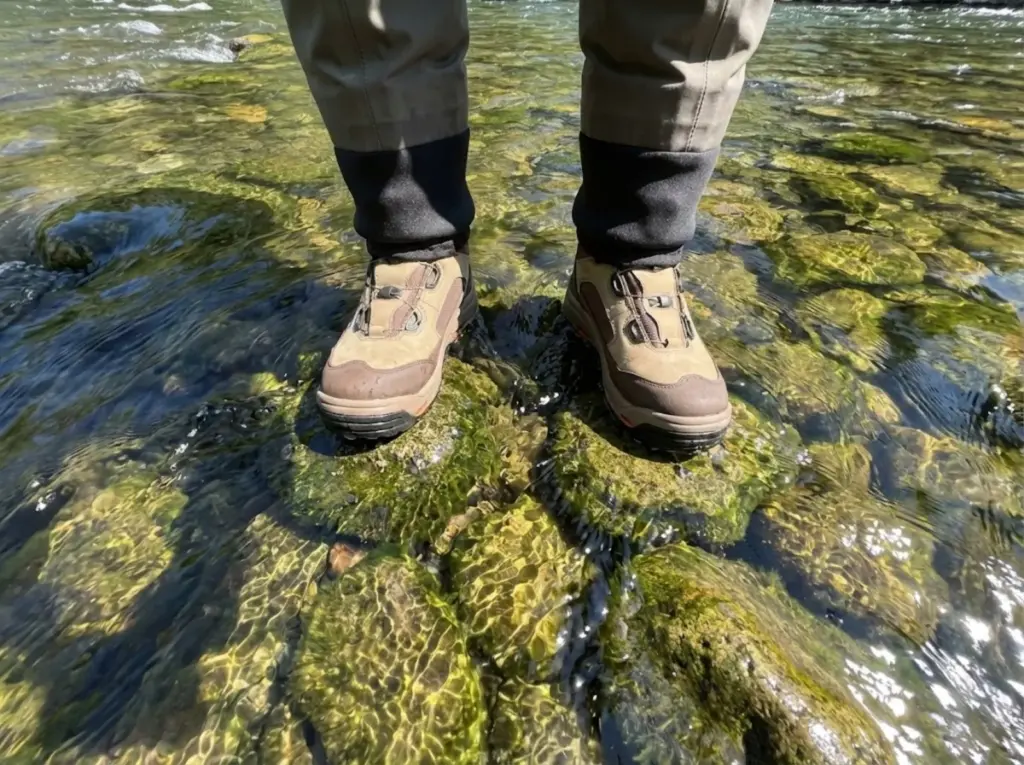 POV view of studded wading boots gripping mossy river rocks in fast current