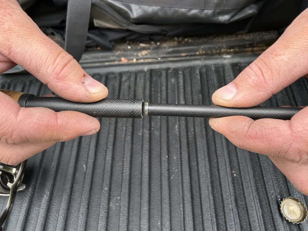 Close-up of a two-piece fishing rod ferrule joint being separated by hand on a tailgate