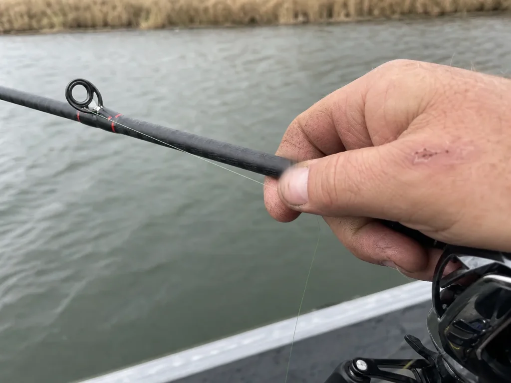 Close-up of an angler's fingers on a casting rod blank feeling for a jig bite on the fall