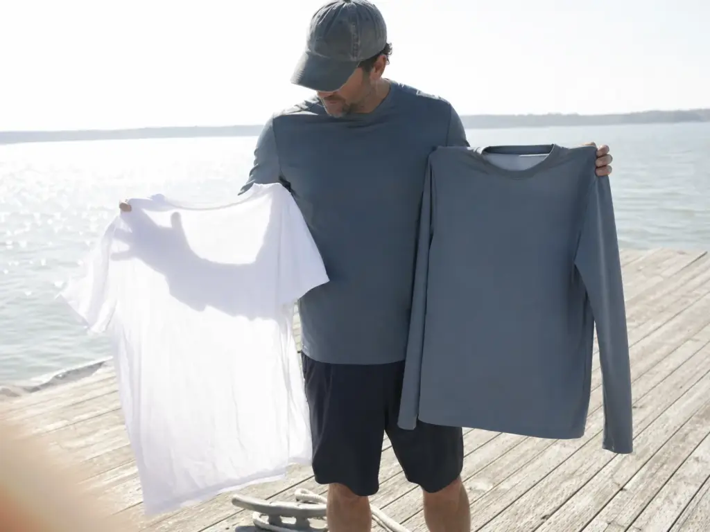 Angler holding a plain cotton tee beside a UPF-rated long-sleeve polyester shirt in direct sunlight