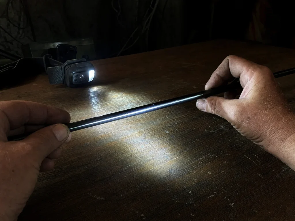 Rotating a rod blank under a focused headlamp beam in the dark to spot a broken light arc from a crack
