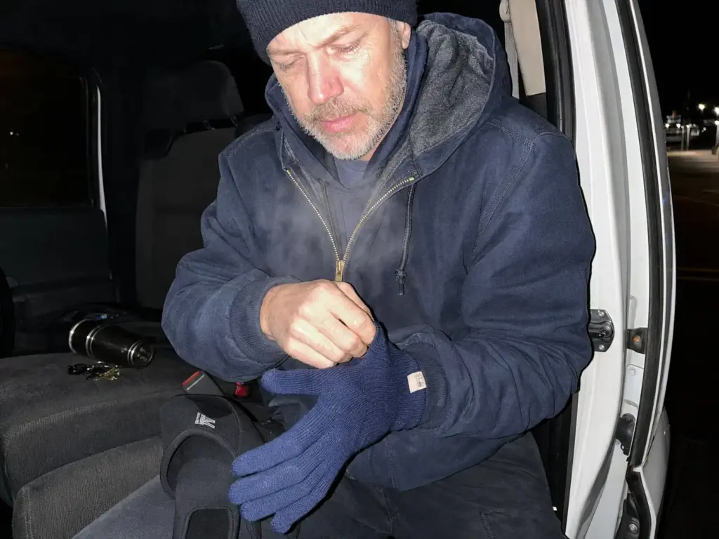 Angler pulling a thin merino liner on before a glove to size the shell one up