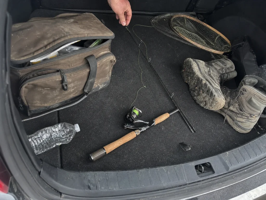 Two-piece fishing rod broken down and laid across a car trunk next to tackle for easy transport