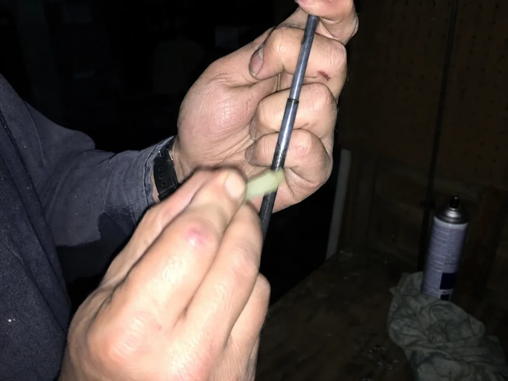 Applying a thin pass of ferrule wax to a two-piece fishing rod joint under harsh flash light