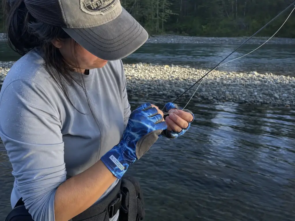 Fingerless fishing gloves letting bare fingertips tie a clinch knot on leader