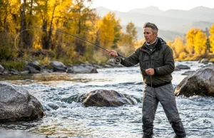 How to Catch Brown Trout in Rivers That Outsmart You Fly angler casting on a fast boulder-strewn river for brown trout at golden hour