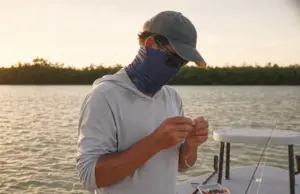 8 Fishing Neck Gaiters Compared One Clear Winner Angler wearing a UPF 50 fishing neck gaiter for sun protection while rigging a rod at dawn