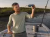 Fishing Sunglasses Lens Color Types Explained Angler holding polarized fishing sunglasses up to the light to check lens color on a skiff deck
