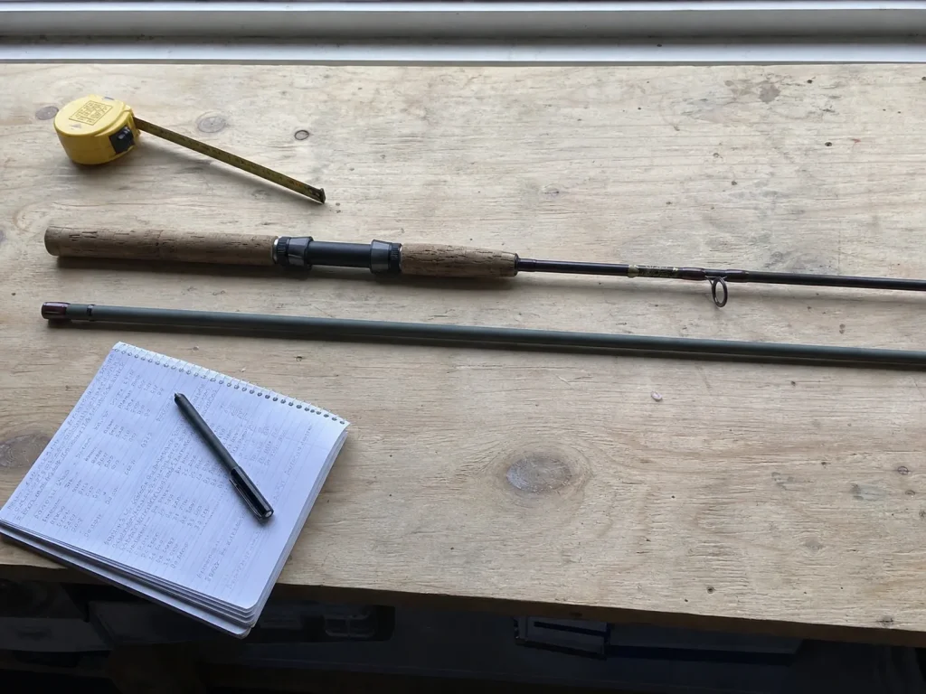 A bare rod blank laid beside a finished factory spinning rod on a workbench for comparison