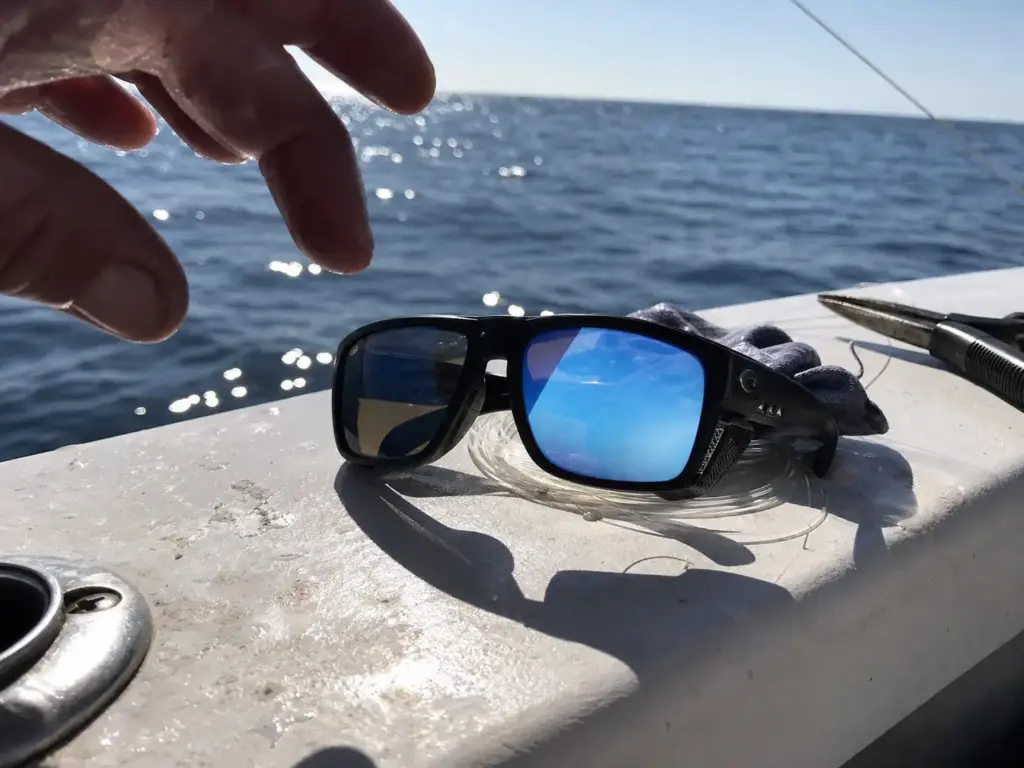 Blue mirror polarized fishing sunglasses resting on a gunwale in bright offshore sun