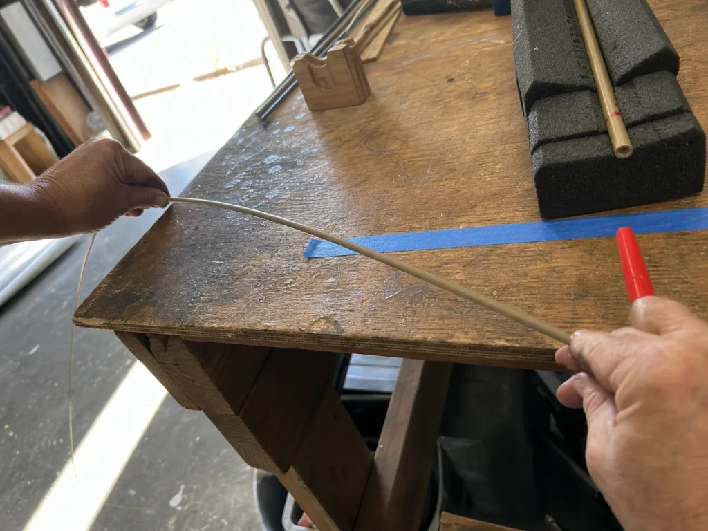 Hands rolling a loaded fishing rod blank across a bench to feel the spine hop before marking it