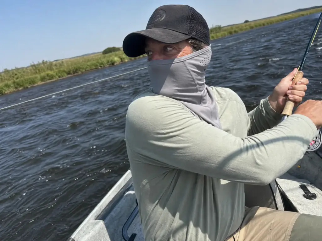 Angler mid hookset with a shaped fishing neck gaiter staying seated over the face