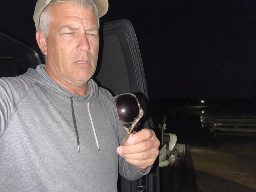 Angler checking a pair of low-light fishing sunglasses at a dark boat ramp before sunrise