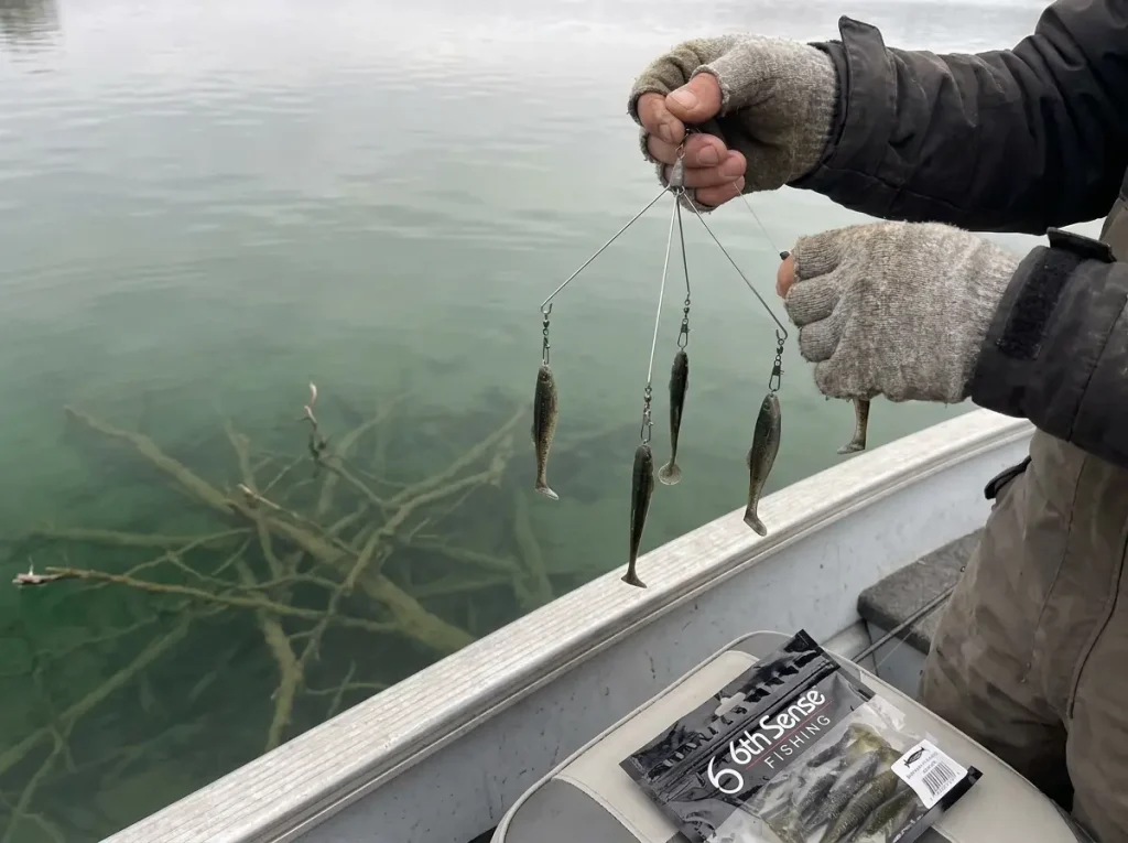 Five-arm Alabama rig with paddle-tail swimbaits attached, held over clear reservoir water with a submerged brush pile visible below
