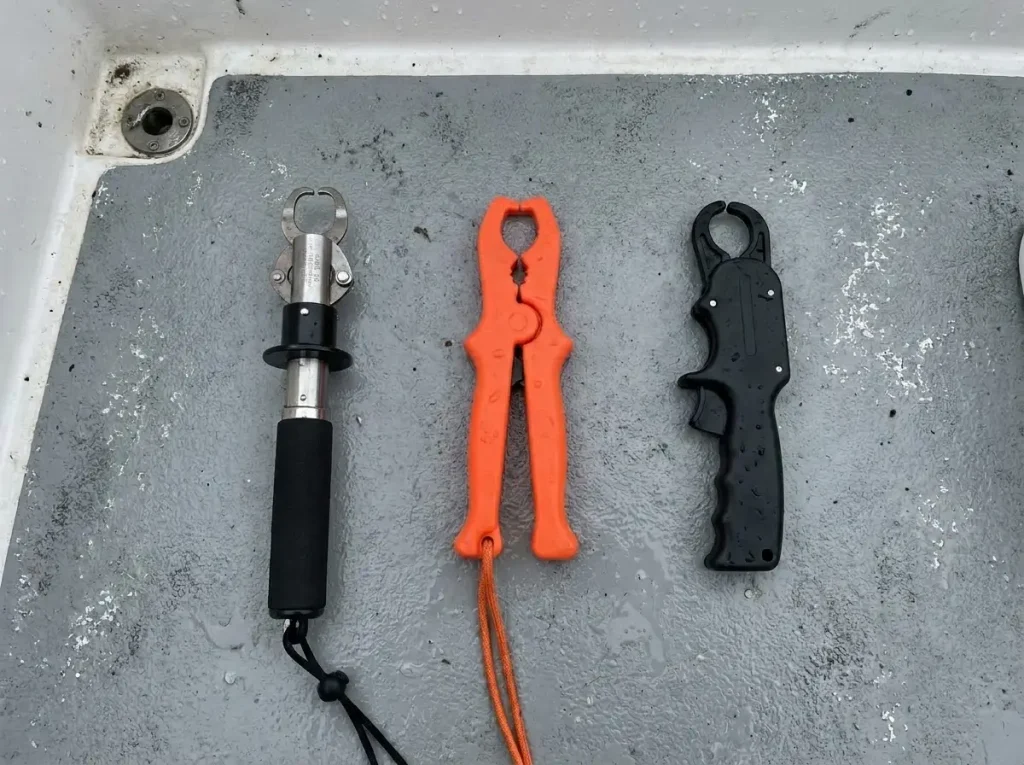 Three fish lip grip tools compared side-by-side on a boat deck: Boga Grip with scale, floating plastic gripper, and pistol grip style
