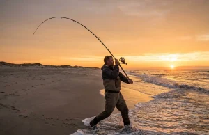 How to Pendulum Cast for Maximum Surf Fishing Distance Surf angler executing a full pendulum cast on a barrier island beach at dawn with a 13-foot rod bent in a full power arc