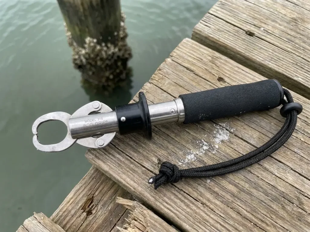 Boga Grip fish handling tool with open jaws and scale dial visible, laid on weathered dock planks