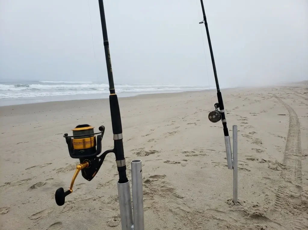 Two surf rods compared side-by-side in beach sand spike holders showing the difference between standard and long-distance surf casting setups