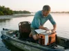 Best Fishing Cooler Bags for Kayak and Offshore Angler loading catch into a fishing cooler bag on a kayak at sunrise to keep the catch fresh