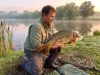 Why Most Anglers Get Common Carp Completely Wrong Angler holding a large common carp near a lake shoreline at dawn