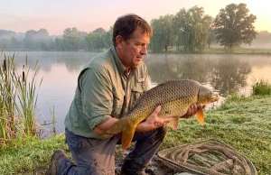 Why Most Anglers Get Common Carp Completely Wrong Angler holding a large common carp near a lake shoreline at dawn