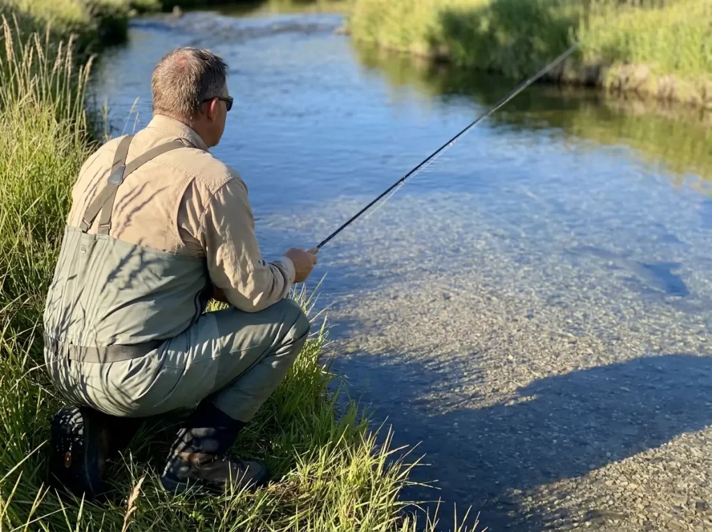 Fly angler making low careful approach to clear river pool to avoid spooking fish