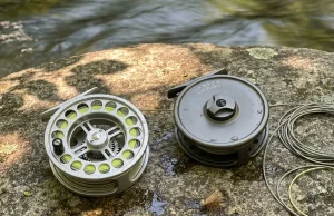 Click Pawl vs Disc Drag Fly Reel What Really Wins Hardy click-pawl fly reel and Lamson disc drag fly reel side by side on streamside rock