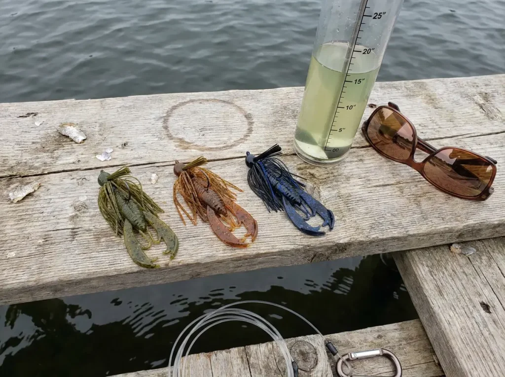 Football jigs in three colors arranged beside a water clarity tube showing turbidity levels