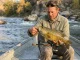 7 Tube Jig Retrieves That Crack Smallmouth Angler holding smallmouth bass caught on tube jig over rocky river, green pumpkin tube visible